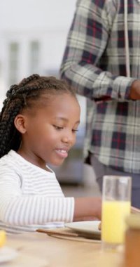 Babasıyla birlikte evde kahvaltı yapan Afrikalı Amerikalı kızın dikey videosu. Ağır çekimde. Ev hayatı, yemek ve yaşam tarzı, değişmemiş..