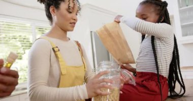 Mutlu Afro-Amerikan ebeveynler ve kızları evde makarnayı kavanoza koyuyorlar, ağır çekimde. Aile hayatı, yemek, aile ve yaşam tarzı, değiştirilmemiş..