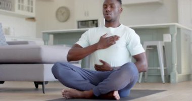 Odaklanmış Afrikalı Amerikalı adam güneşli oturma odasında yoga meditasyonu yapıyor, ağır çekimde. Ev, refah, zindelik ve sağlıklı yaşam tarzı, değişmemiş..