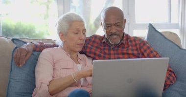 Kanepede oturan ve laptoplarını yavaş çekimde kullanan mutlu çift. Ev hayatı, emeklilik, teknoloji ve yaşam tarzı, değişmedi..