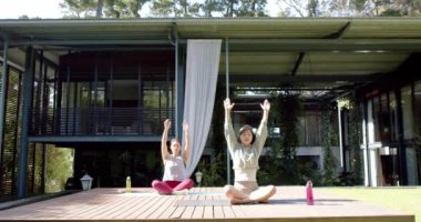 Odaklanmış Asyalı bayan arkadaşlar güneşli terasta yoga meditasyonu yapıyorlar, yavaş çekim. Sağlıklı yaşam tarzı, zindelik ve refah, arkadaşlık, değişmemiş.