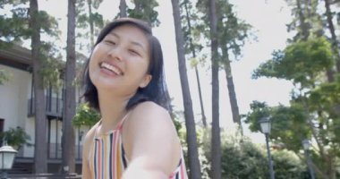 Mutlu Asyalı kadın arkasını dönüyor ve güneşli bahçede gülümsüyor, ağır çekim. Yaz, tatil, doğa, refah, değişmemiş.