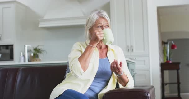 Χαρούμενη Καυκάσια Ηλικιωμένη Γυναίκα Πίνει Καφέ Και Χαμογελά Στον Καναπέ — Αρχείο Βίντεο
