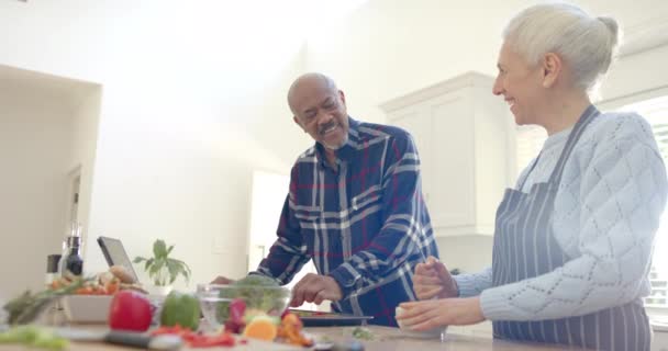 ハッピー多様なシニアカップルは野菜を準備し キッチンでタブレットを使用しています スローモーション コミュニケーション 家庭生活 食べ物 健康的なライフスタイル — ストック動画