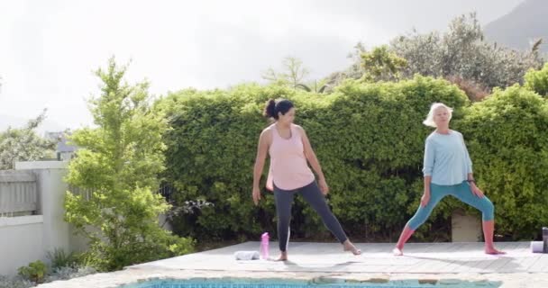 晴れた庭のプールでヨガを練習する2人の幸せな多様なシニア女性 ゆっくりとした動き コピースペース フィットネス 家庭生活 シニアライフスタイル 変わらない — ストック動画