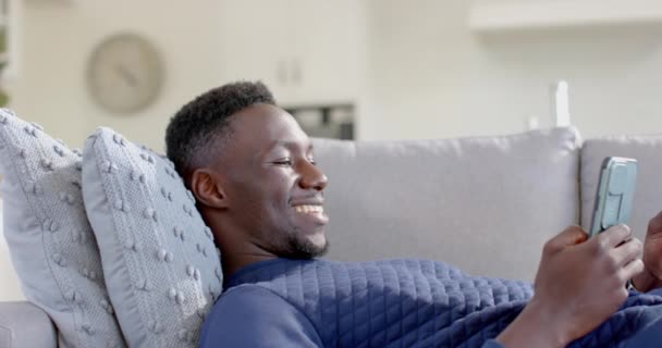 快乐的非洲裔美国人在阳光灿烂的客厅里用智能手机和信用卡 慢动作 Home Domestic Life Lifestyle Wellbeing Communication Technology Finance — 图库视频影像