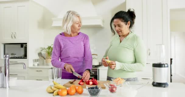 两个快乐多样的老年妇女在厨房切水果 在厨房笑 动作缓慢 家庭生活 老年和健康的生活方式 — 图库视频影像