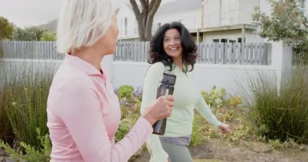 Zwei Unterschiedliche Seniorinnen Gehen Mit Wasserflaschen Spazieren Und Unterhalten Sich — Stockvideo