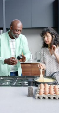 Çift ırklı mutlu çiftin kahvaltıyı hazırlarken çekilmiş dikey videosu, yavaş çekim. Ev hayatı, yemek pişirme ve yaşam tarzı, değişmemiş..