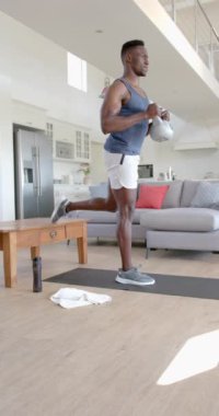 Odaklanmış Afro-Amerikan bir adam güneşli oturma odasında kettlebell ile egzersiz yapıyor, ağır çekimde. Ev, egzersiz, fitness ve sağlıklı yaşam tarzı, değişmemiş..