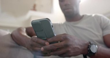 Mutlu Afro-Amerikan erkek askeri akıllı telefon kullanıyor ve güneşli oturma odasında gülüyor, ağır çekimde. Askerlik, ordu, boş zaman ve ev hayatı, iletişim, değişmemiş.