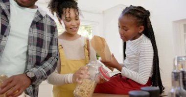 Mutlu Afro-Amerikan ebeveynler ve kızları evde makarnayı kavanoza koyuyorlar, ağır çekimde. Aile hayatı, yemek, aile ve yaşam tarzı, değiştirilmemiş..