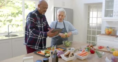 Mutfakta tablet, kopyalama alanı ve ağır çekim kullanarak sebze hazırlayan mutlu yaşlı çift. İletişim, ev hayatı, yemek pişirme, emeklilik ve sağlıklı yaşam tarzı, değişmedi..