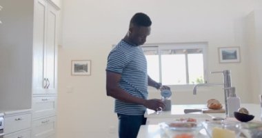 Mutlu Afro-Amerikalı bir adam kahvesini güneşli mutfakta içiyor, ağır çekimde. Ev, ev hayatı, yaşam tarzı, yemek, rahatlama, değişmemiş.