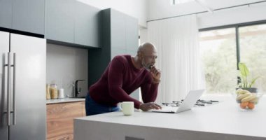 Mutfakta dizüstü bilgisayar kullanan, iki ırklı, mutlu bir adam, ağır çekimde. Ev hayatı, iletişim, teknoloji ve yaşam tarzı, değişmedi..