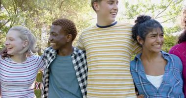 Sunny Park 'ta kucaklaşan mutlu genç arkadaş grubunun portresi, yavaş çekim. Gen z, arkadaşlık, takılma, doğa ve yaşam tarzı, değişmemiş.