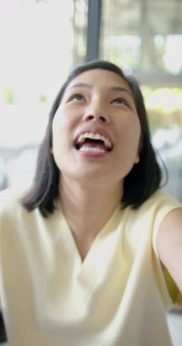 Mutlu Asyalı kadın, güneşli oturma odasında kamerayla konuşuyor ve gülümsüyor, ağır çekimde. Yaşam tarzı, iletişim, teknoloji ve ev hayatı, değişmedi..