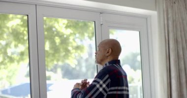Düşünceli kıdemli çift ırklı adam, pencereden eve bakıyor, ağır çekimde. Ev hayatı, emeklilik ve yaşam tarzı, değişmedi..