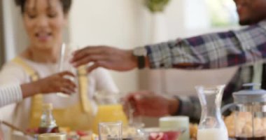 Mutlu Afro-Amerikan ebeveynler ve kızları kahvaltılarını evde yapıyorlar, ağır çekimde. Aile hayatı, yemek, aile ve yaşam tarzı, değiştirilmemiş..