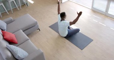 Odaklanmış Afrikalı Amerikalı adam güneşli oturma odasında yoga meditasyonu yapıyor, ağır çekimde. Ev, refah, zindelik ve sağlıklı yaşam tarzı, değişmemiş..