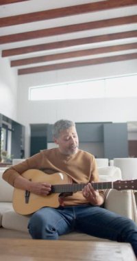 Yaşlı, çift ırklı bir adamın gitar çalıp evde şarkı söylediği dikey bir video. Müzik, boş zaman, hobiler, rahatlama, yaratıcılık, ev hayatı ve son sınıf yaşam tarzı, değiştirilmemiş.