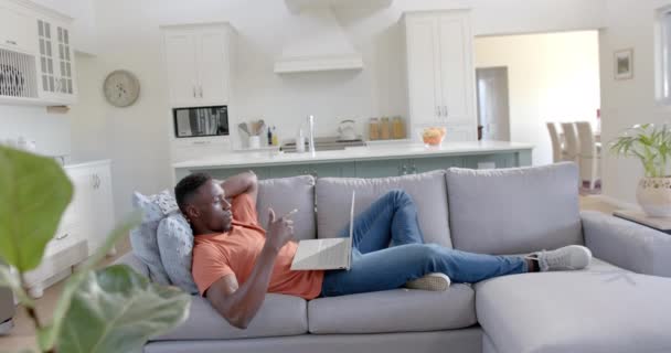 ハッピーなアフリカ系アメリカ人男性が 日当たりの良いリビングルームでラップトップでビデオ通話をして ゆっくり動く ホーム 家庭生活 ライフスタイル コミュニケーション テクノロジー 変更されていない — ストック動画