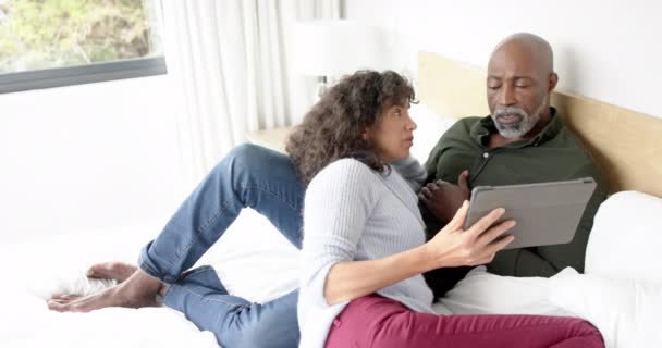 幸せな成熟した多様なカップルは タブレットを使用してベッドに座って 自宅で話す 遅い動き 国内生活 コミュニケーション テクノロジー ライフスタイル — ストック動画