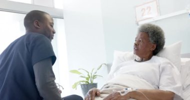Afrika kökenli Amerikalı erkek doktor hastane odasında kadın kıdemli hastayla konuşuyor, ağır çekimde. İlaç, sağlık ve sağlık hizmetleri, değiştirilmemiş.