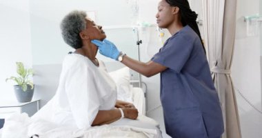 Afrika kökenli Amerikalı kadın doktor hastane odasında yaşlı kadın hastanın boynunu yavaş çekimde test ediyor. İlaç, sağlık ve sağlık hizmetleri, değiştirilmemiş.