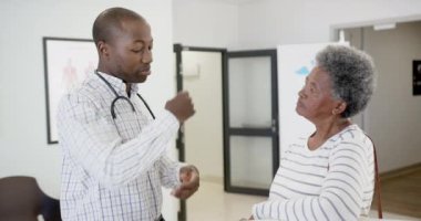Afrika kökenli Amerikalı erkek doktor hastanede yaşlı bir kadınla konuşuyor, ağır çekimde. İlaç, sağlık ve sağlık hizmetleri, değiştirilmemiş.