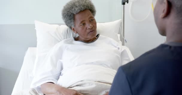 非洲裔美国男性医生在病房里与老年女性病人交谈 动作缓慢 保健和医疗服务 未加改动 — 图库视频影像
