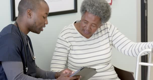 アフリカ系アメリカ人の男性医師がタブレットを使用し 病院のシニア女性と話し 動きが遅い ヘルスケア コミュニケーション 医療サービス 変わらない — ストック動画