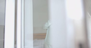 Yatak odasının penceresinden dışarı bakan düşünceli, melez bir kadın, kopyalama alanı, ağır çekim. Günaydın, ev hayatı ve sağlıklı yaşam tarzı, değişmemiş..