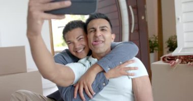 Yeni eve taşınan mutlu eşcinsel çift oturma odasında selfie çekiyorlar, ağır çekimde. İletişim, ev, taşınma evi, gay, birliktelik, ev hayatı ve yaşam tarzı, değişmemiş.