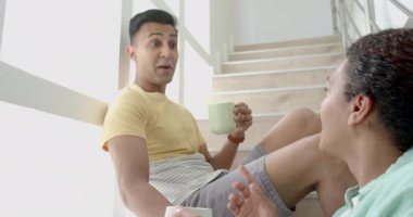 Mutlu eşcinsel çift, güneşli merdivenlerde oturup kahve içip sohbet ediyorlar, ağır çekim. Rahatlama, ev, gay, ilişki, birliktelik, ev hayatı ve yaşam tarzı, değişmemiş.