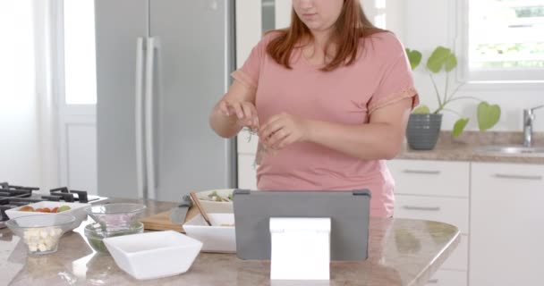 キッチンで野菜サラダを作るハッピープラスサイズの女性とタブレットを使用して スローモーション コミュニケーション レシピ 食べ物 家庭生活 健康的なライフスタイル — ストック動画