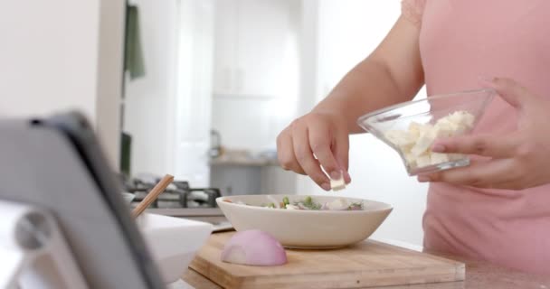 キッチンでサラダを作るハッピープラスサイズの女性とタブレットを使用して スローモーション コミュニケーション レシピ 食べ物 家庭生活 健康的なライフスタイル — ストック動画