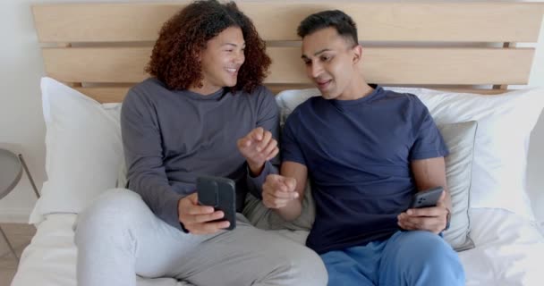 Happy Diverse Gay Male Couple Sitting Bed Using Smartphones Talking — Stock Video