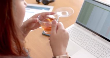 Diz üstü bilgisayar kullanırken çay içen, evde çalışan, ağır çekimde odaklanmış, melez bir kadın. Uzaktan çalışma, iletişim, ev hayatı ve yaşam tarzı, değiştirilmemiş.