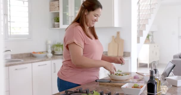 ハッピープラスサイズの女性はキッチンで野菜と食事をし タブレットを使用して ゆっくり動作します コミュニケーション レシピ 食べ物 家庭生活 健康的なライフスタイル — ストック動画