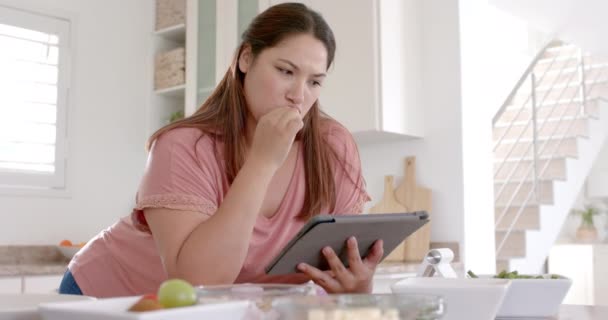 ハッピープラスサイズの女性は タブレットを使用してキッチンで食事をし フルーツを食べて ゆっくり動きます コミュニケーション レシピ 食べ物 家庭生活 健康的なライフスタイル — ストック動画