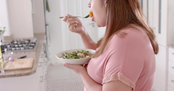 キッチンで野菜サラダを食べるハッピープラスサイズの女性 スローモーション クッキング 食べ物 家庭生活 健康的なライフスタイル — ストック動画