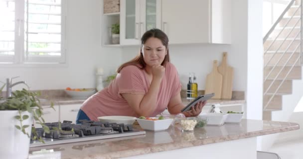 ハッピープラスサイズの女性はキッチンで野菜と食事をし タブレットを使用して ゆっくり動作します コミュニケーション レシピ 食べ物 家庭生活 健康的なライフスタイル — ストック動画