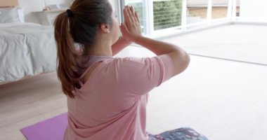 Odaklanmış ve çift ırklı bir kadın yatak odasında oturmuş yoga meditasyonu yapıyor, ağır çekimde. Lotus pozisyonu, yoga, meditasyon, refah, ev hayatı ve sağlıklı yaşam tarzı, değişmemiş.