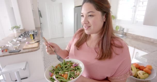 快乐加大小的比利卡女人站在厨房里吃蔬菜沙拉 动作缓慢 家庭生活和健康的生活方式 — 图库视频影像