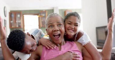 Mutlu Afro-Amerikan torunları, büyükannelerini kanepede kucaklıyor, ağır çekimde. Yaz, çocukluk, aile, birliktelik, ev hayatı ve yaşam tarzı, değişmemiş..