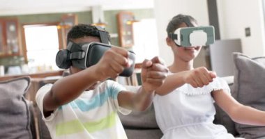 Afro-Amerikan erkek ve kız kardeşleriniz kanepelerde ağır çekimde kulaklık kullanırken mutlu olun. Yaz, çocukluk, birliktelik, iletişim, dijital arayüz, teknoloji, ev hayatı ve yaşam tarzı, değiştirilmemiş.