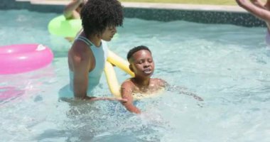 Mutlu Afro-Amerikan annesi oğluna güneşli havuzda erişte yüzmesini öğretiyor, ağır çekimde. Yaz, aile, öğrenme, yüzme, eğlence, birliktelik, tatiller, boş zaman ve yaşam tarzı, değişmemiş.