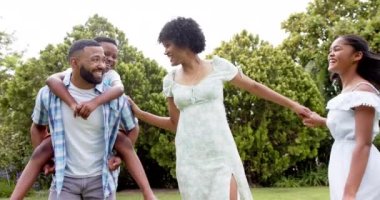 Mutlu Afro-Amerikan ebeveynler, kız ve oğul bahçede sırtına binip dans ediyor, ağır çekimde. Çocukluk, aile, eğlence, boş zaman, birliktelik ve yaşam tarzı, değişmemiş..
