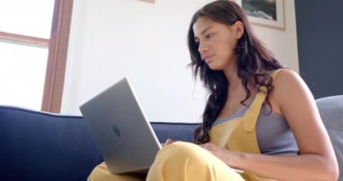 Dizüstü bilgisayar kullanarak kanepede oturan mutlu çift ırklı genç kız, yavaş çekim. İletişim, teknoloji, çalışmalar, ergenlik, ev hayatı ve yaşam tarzı, değişmemiş.